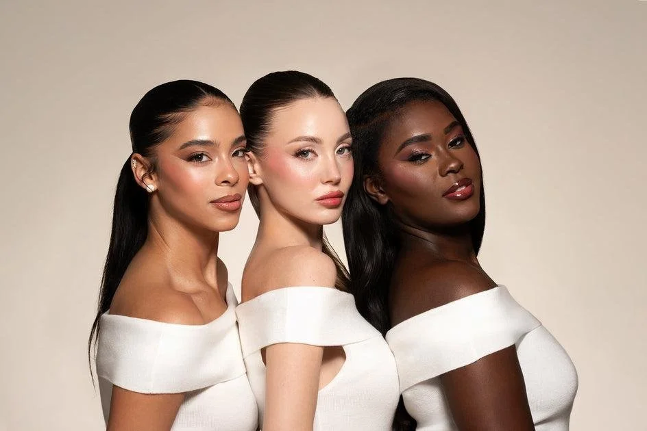 Three women with diverse skin tones smiling together in a welcoming setting