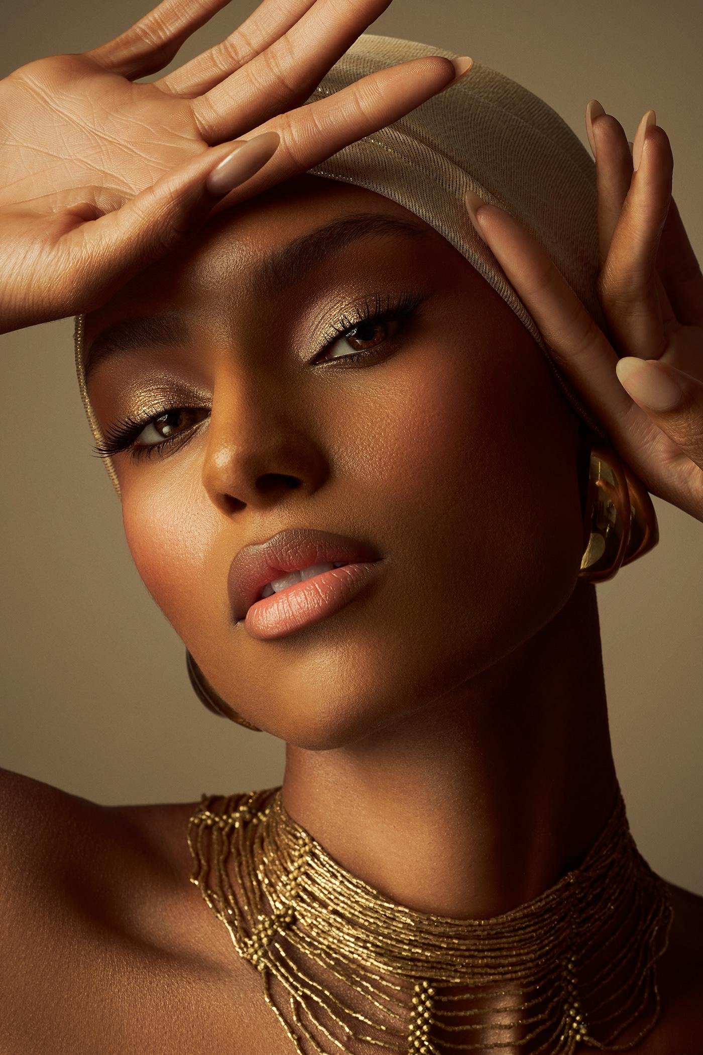 Editorial beauty portrait of a woman wearing a headwrap and layered gold jewelry.