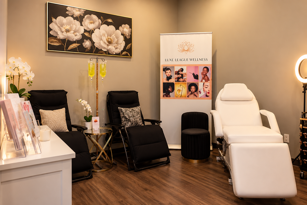Interior of Luxe League Wellness with black IV lounge chairs, a white treatment chair, IV stand, floral wall art, and branded display