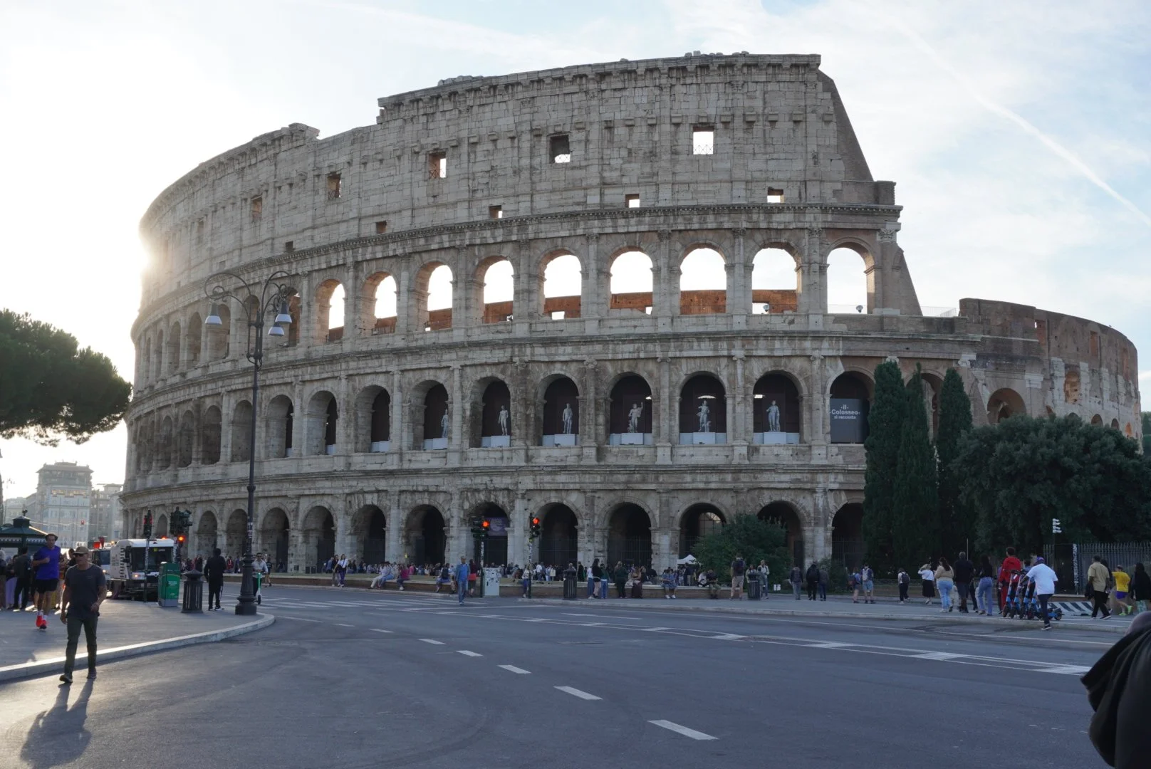 The Roman Colosseum in Rome, Italy, with tourists walking nearby and a street in the foreground.