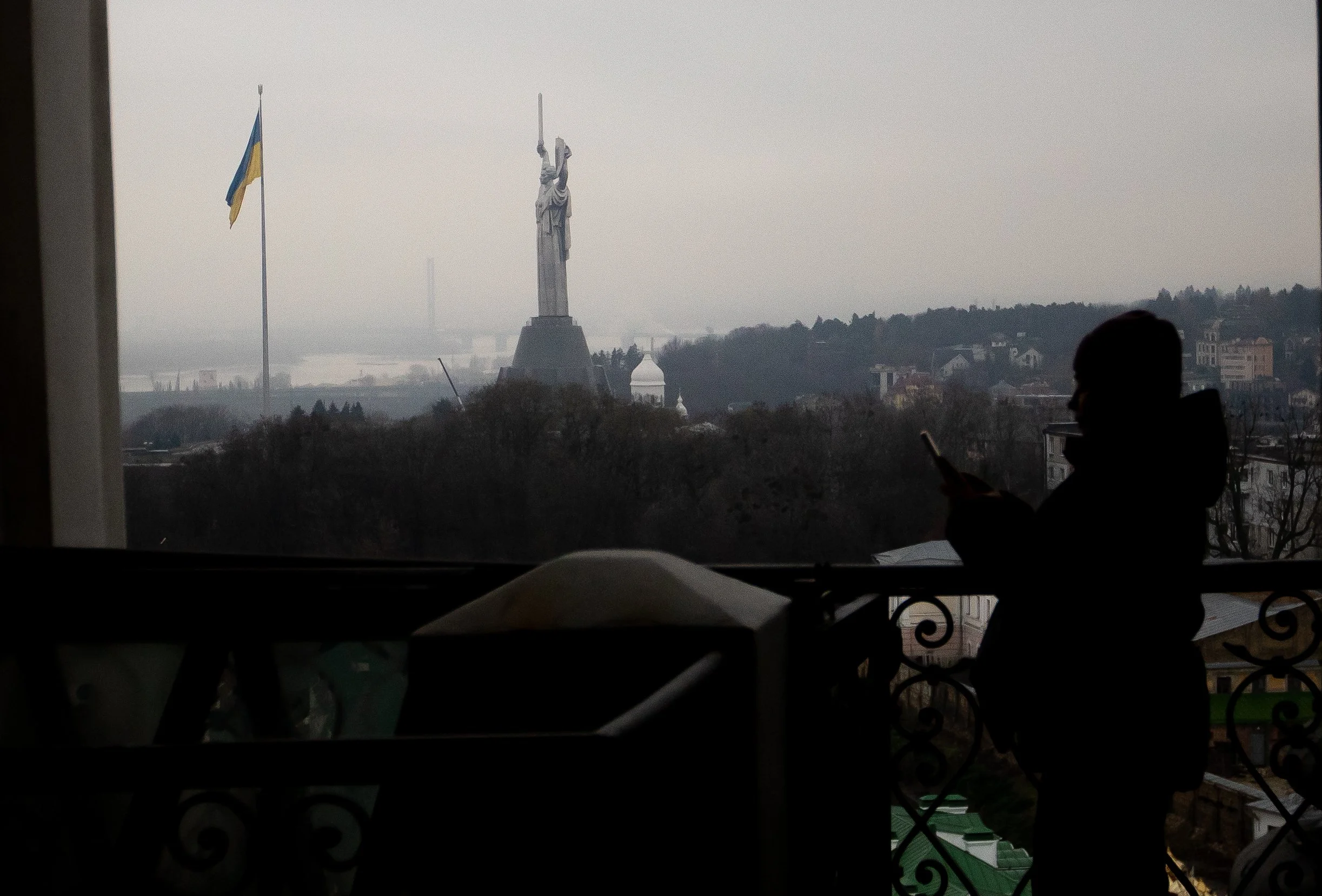 The Ukrainian Motherland Monument, known as “Mother,” sits behind a visitor looking at her phone inside a bell tower at the Kyiv Pechersk Lavra on Nov. 27, 2025.