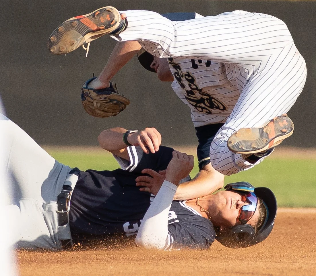 A baseball player in a black uniform and helmet is sliding into a base while another player in a white pinstripe uniform and helmet is trying to tag him out.