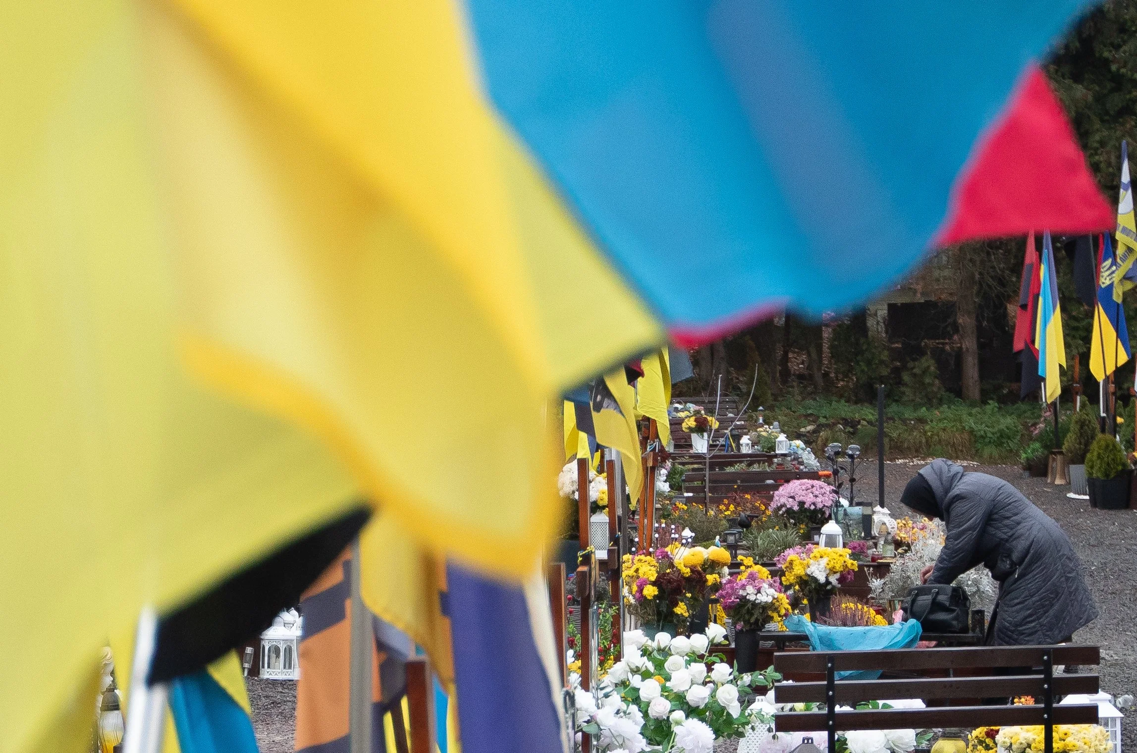 A woman grieves over the grave of a soldier Nov. 20, 2025 in Lviv, Ukraine as flags wave in the wind.