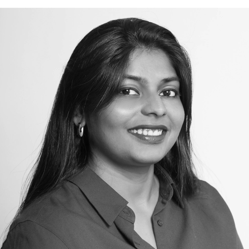 Black and white portrait of a woman with long dark hair, smiling, wearing a collared shirt and hoop earrings. Sherin Samuel
