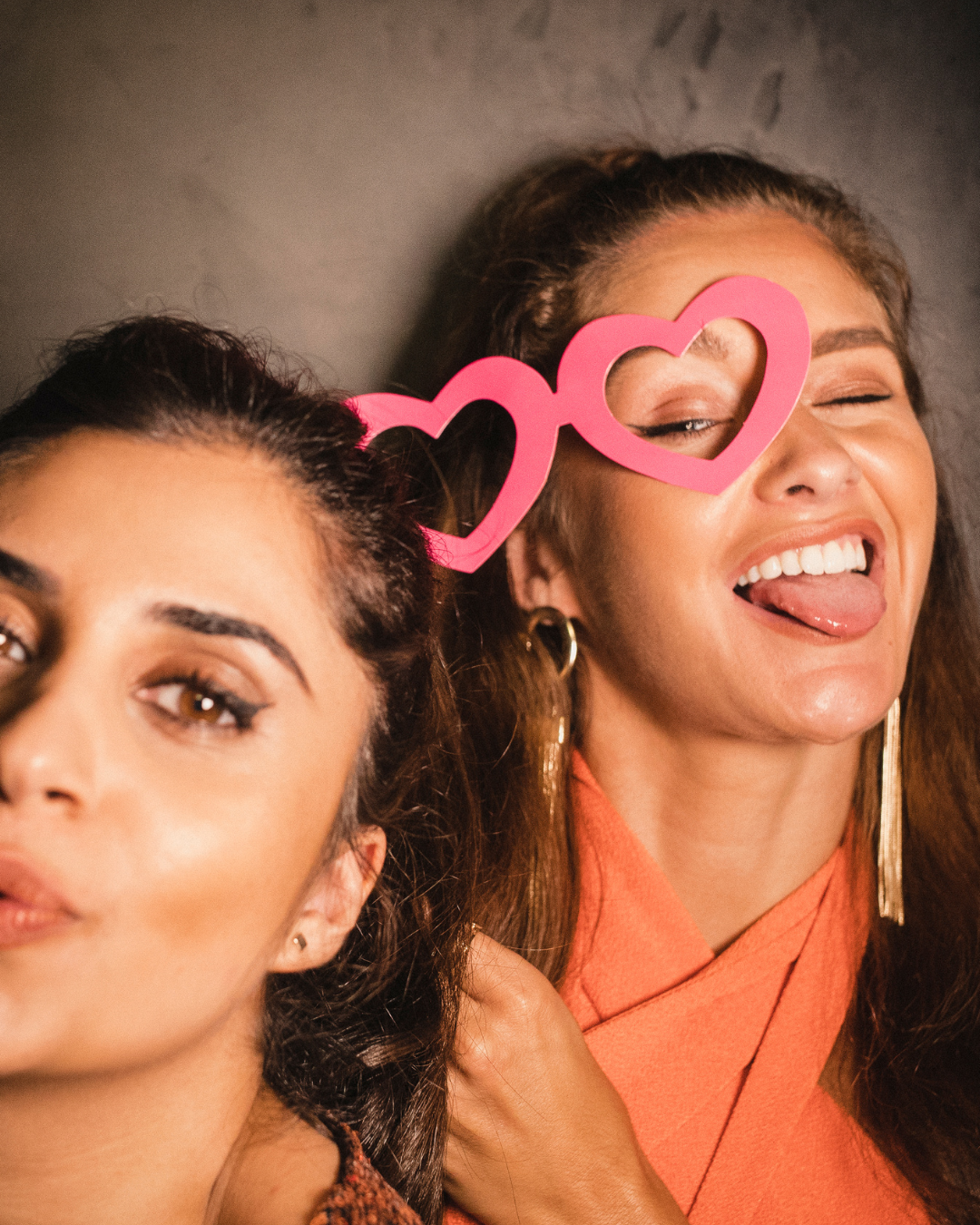 Two women lying down with pink heart-shaped glasses, one is winking and sticking out her tongue, both smiling. Bridesmaid Bachelorette party Ottawa