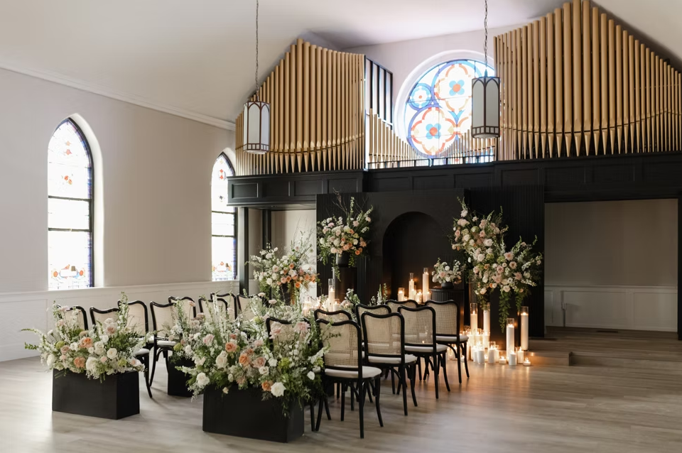 Elegant wedding event ceremony setup with floral arrangements, candles, and arched stained glass windows in a bright room at Two Cross Commons in Elmira, Ontario