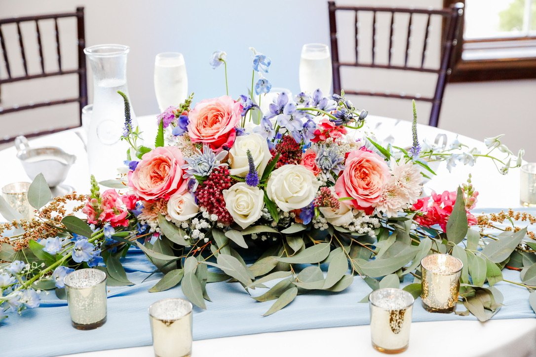 Elegant floral centerpiece with pink and white roses, purple and pink flowers, surrounded by candles on a dining table