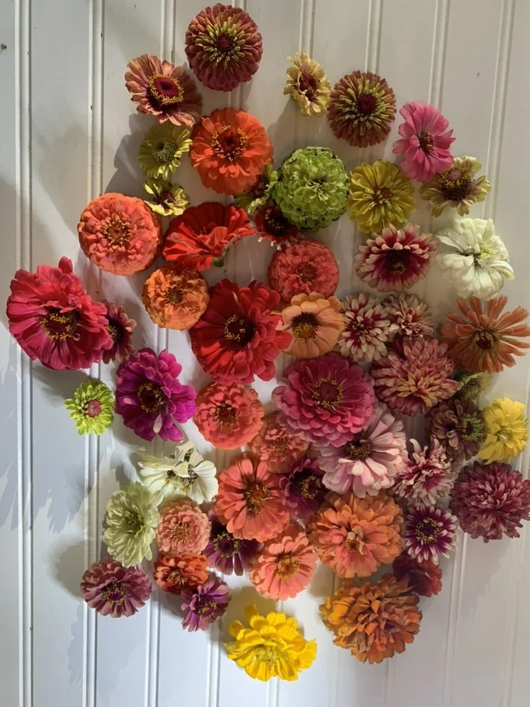 A decorative wall hanging made of colorful artificial flowers arranged on a white wooden panel background.