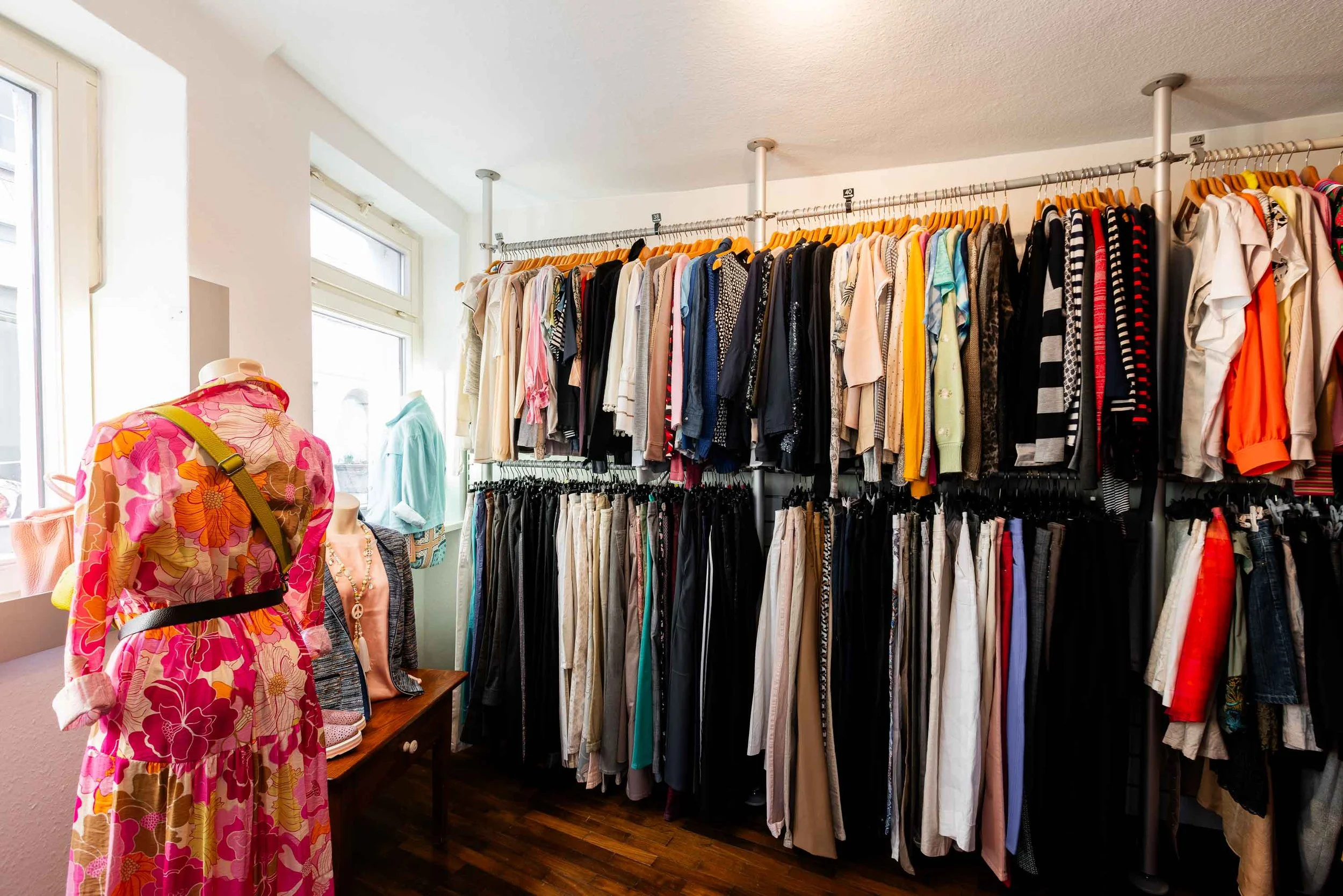 Innenansicht der Boutique mit Kleiderstangen voller Kleidung und einer Schaufensterpuppe.