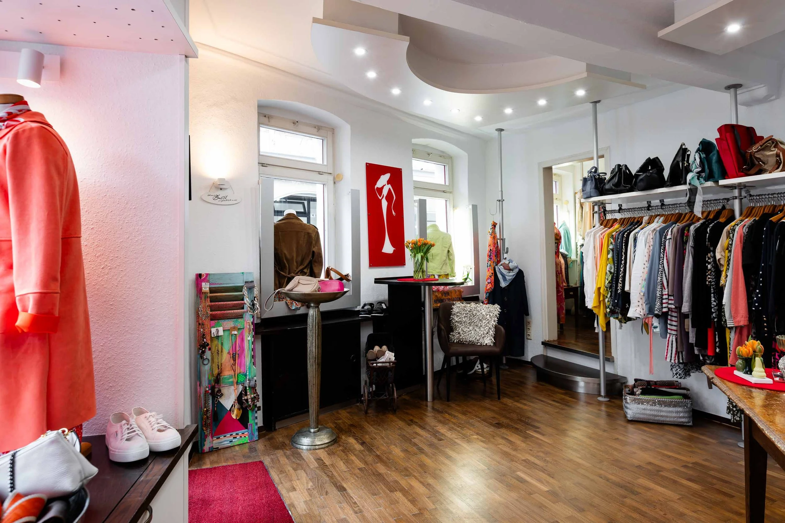 Innenansicht der Boutique Der Besondere Laden mit Designer-Second-Hand-Kleidung, Kleiderstangen, Regalen und großen Fenstern.