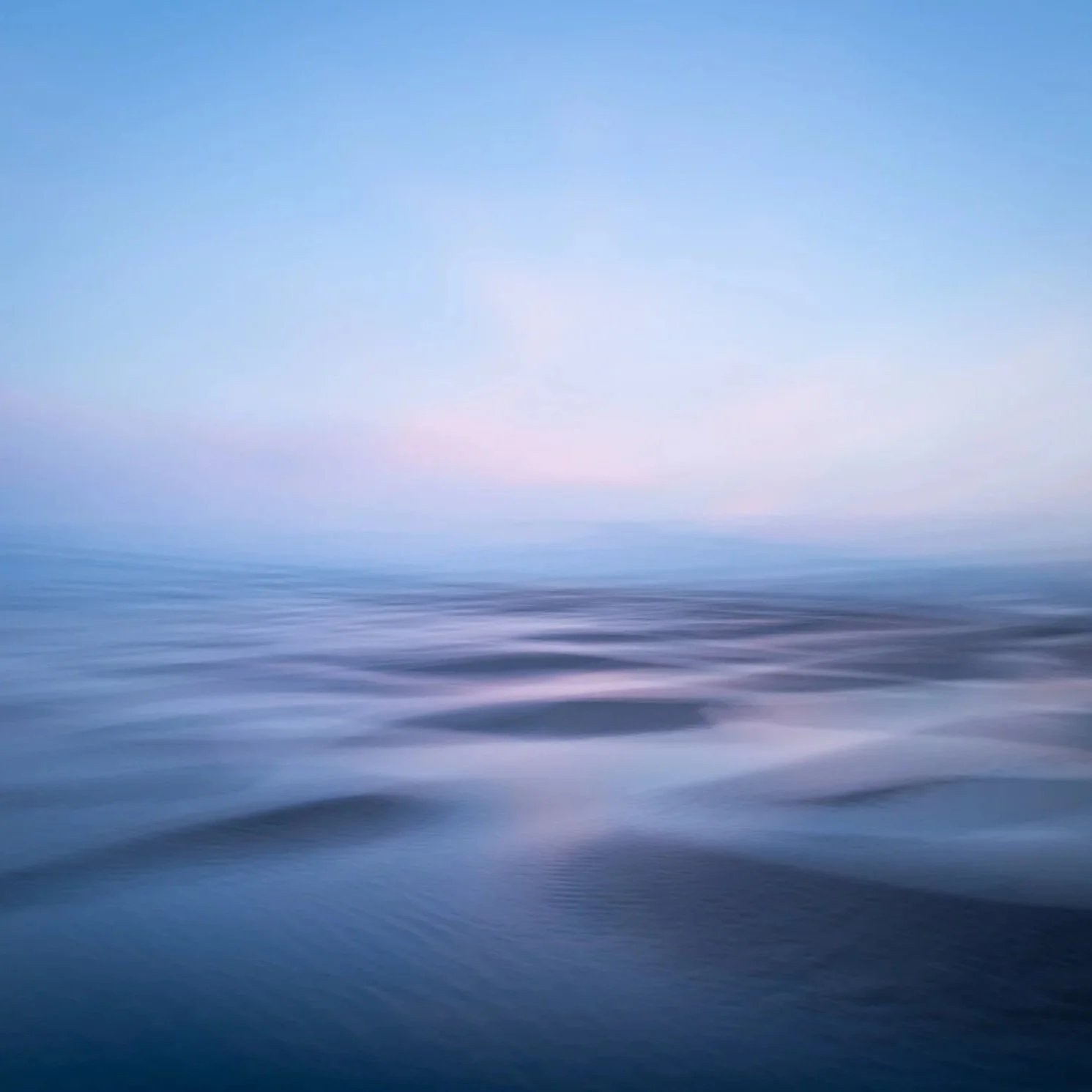 Blurred image of calm water under a clear sky during sunset or sunrise
