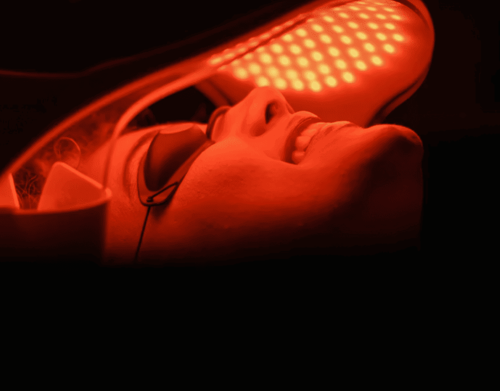 A person lying down under red LED light therapy, with their eyes closed and a relaxed expression.