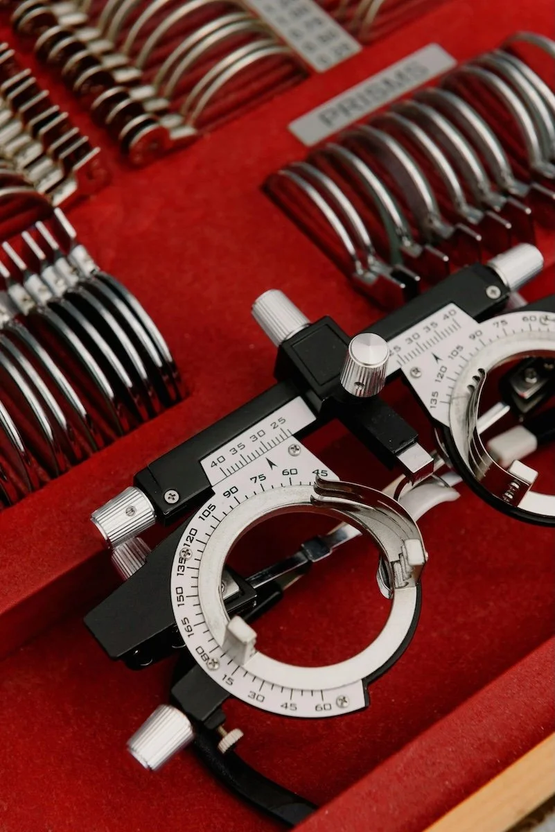 A trial frame optometry device on a red surface with various lenses in the background.