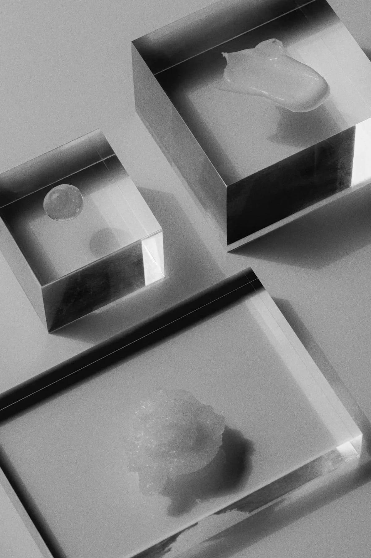 Three reflective metallic boxes with rounded edges, each containing a different object: a small ball, a blob of some substance, and a strawberry on a reflective surface.