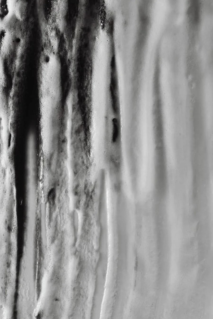 Close-up of a soapy shower wall with foam and water streaks.