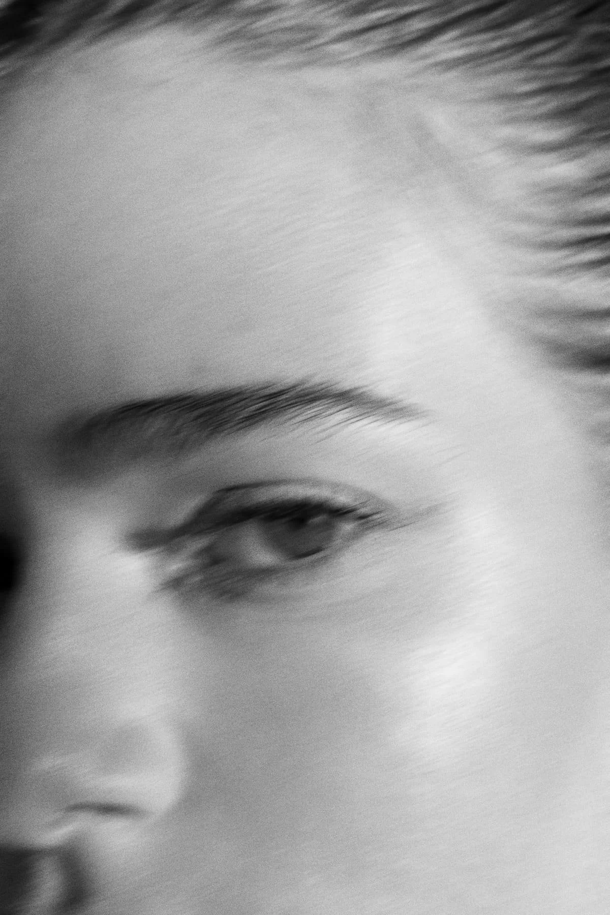 Close-up black and white photo of a person's face, focusing on an eye and part of the eyebrow.