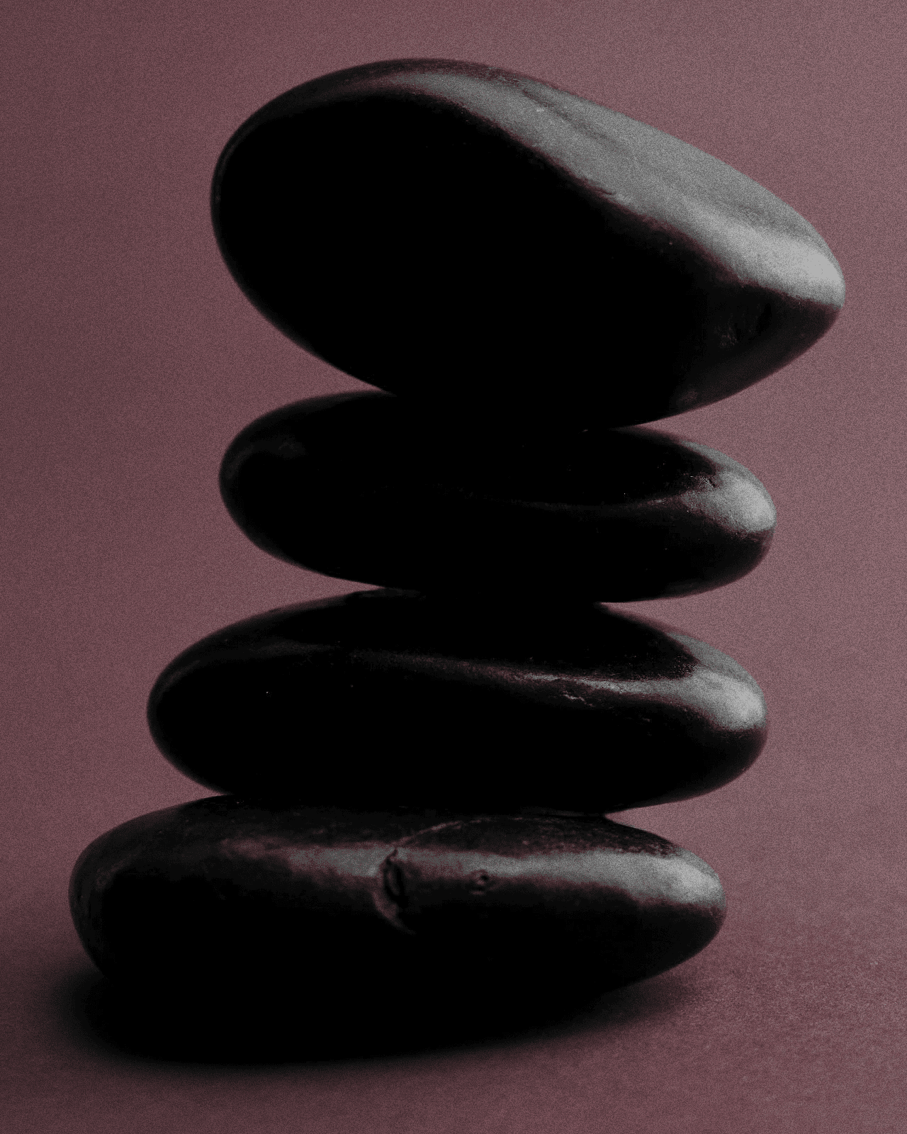Stack of five black massage stones on a purple background.