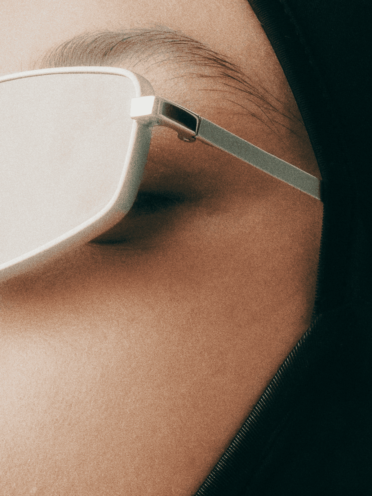 Close-up of a person's eye wearing white sunglasses with metallic arms and dark lenses, with visible eyebrow and skin around the eye.