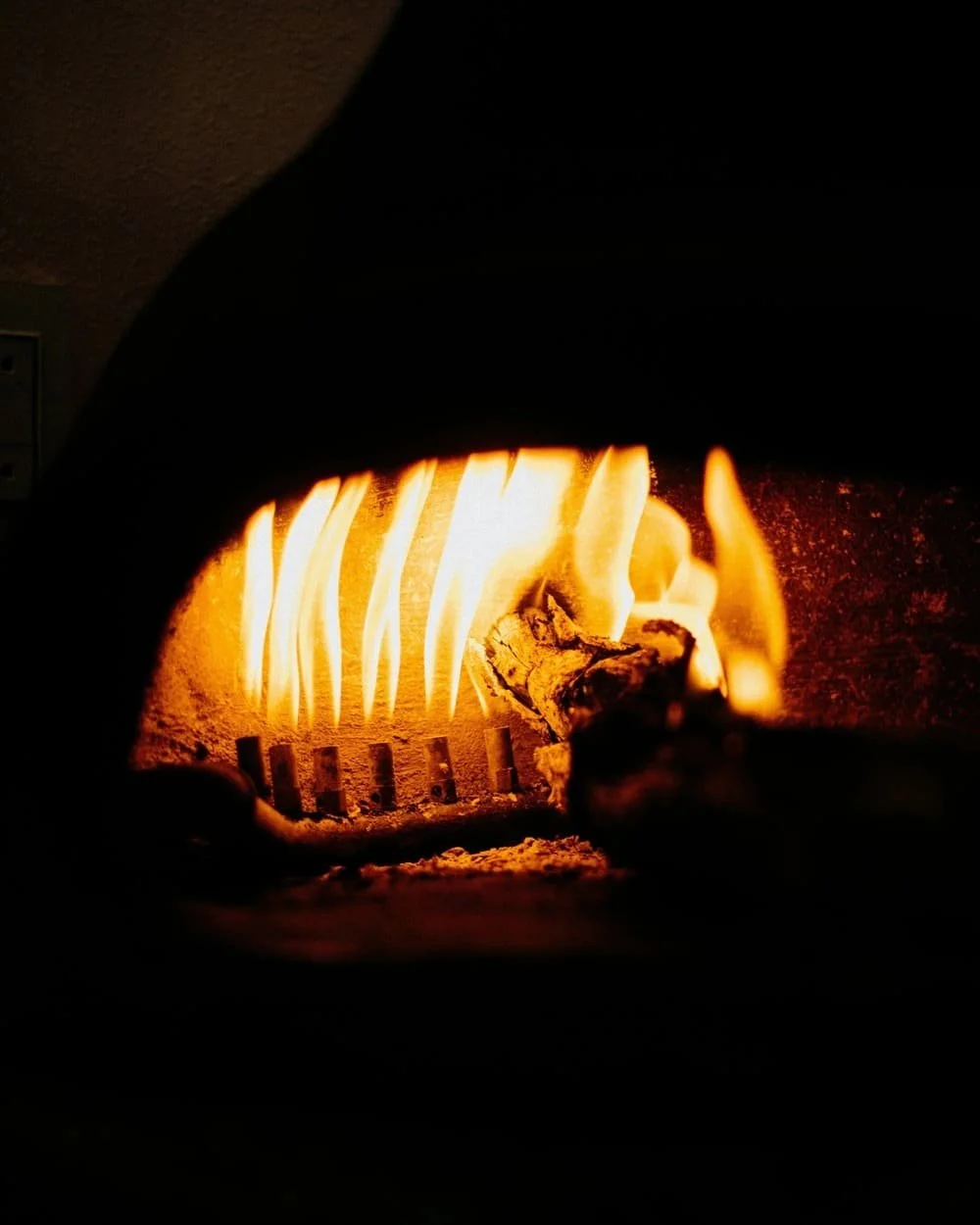 A close-up of a wood-burning stove with flames and burning logs inside.