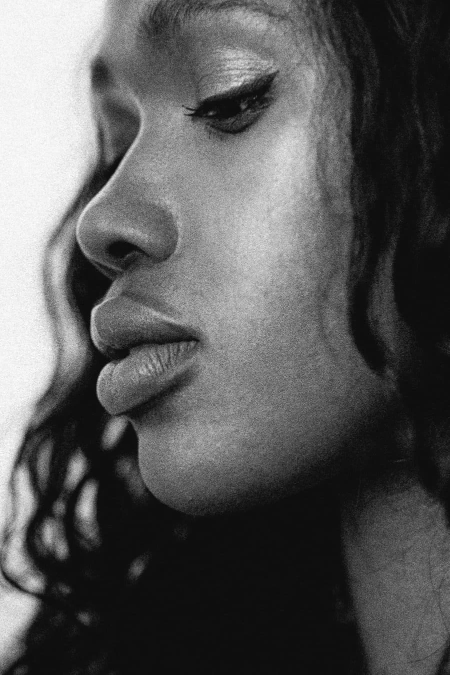 Close-up black-and-white photo of a woman's face in profile, showing her eye, nose, lips, and curly hair.