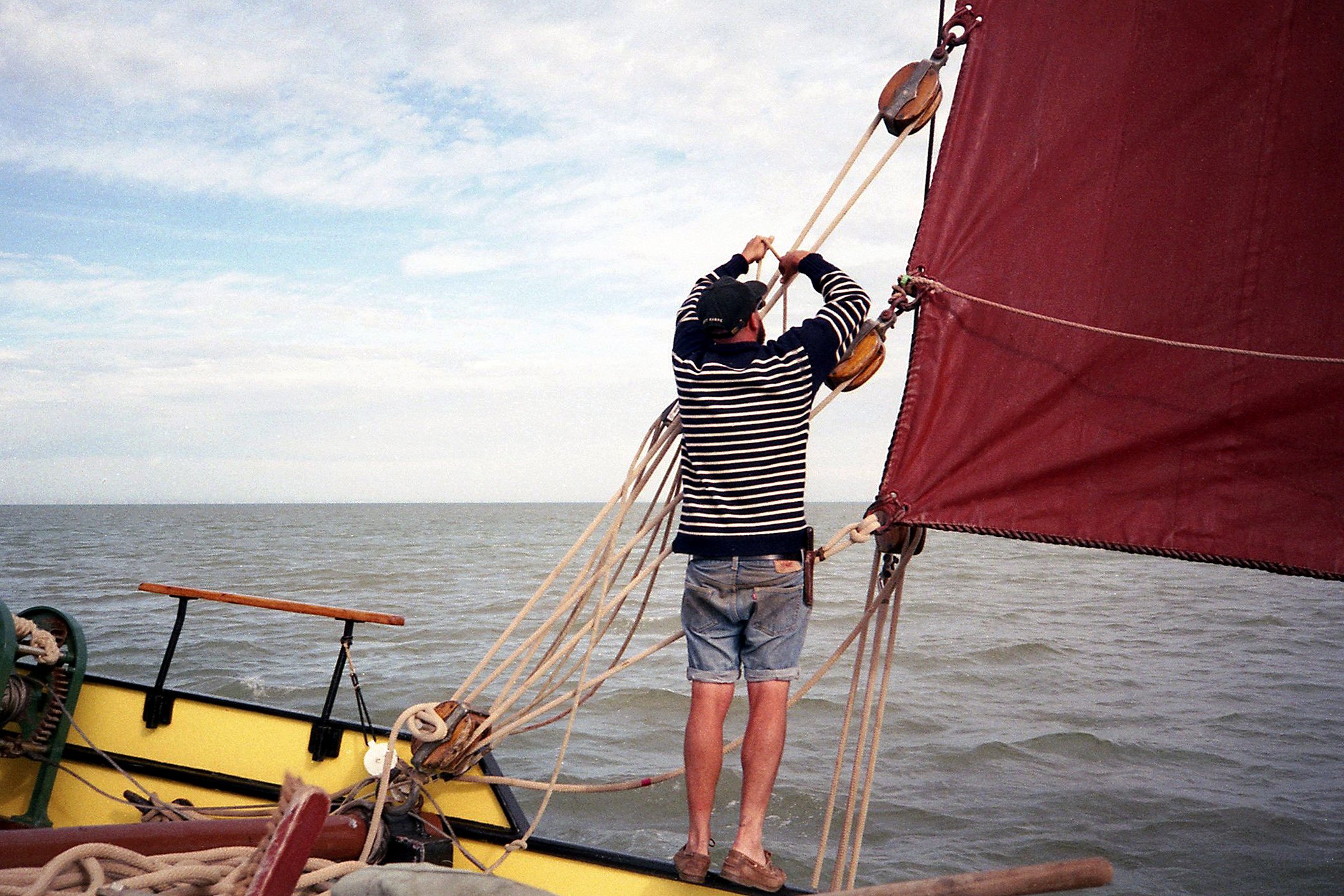A man standing on a Thames Barge, adjusting the main sail in the Thames Barge