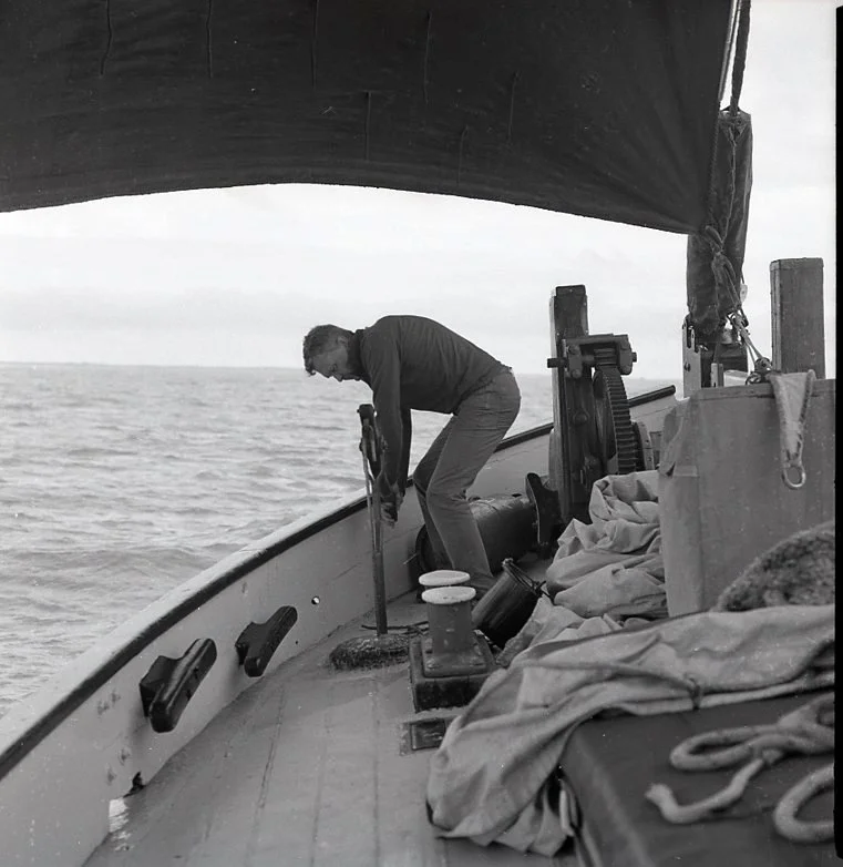 A person cleaning the deck of a boat while out on open water, with the horizon visible in the background.