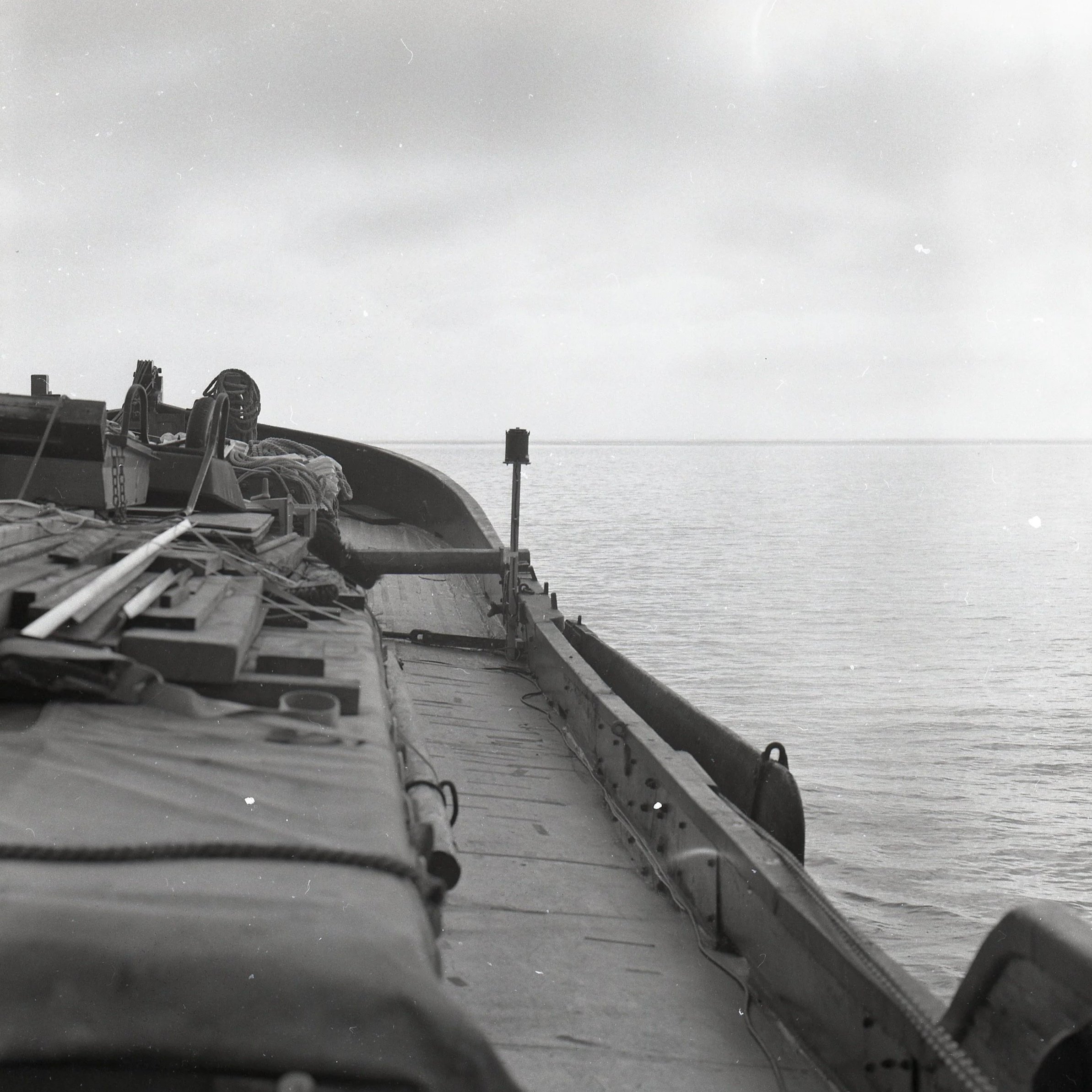 View from the front of a boat looking toward the water, with equipment and ropes on the deck, and a horizon in the distance.