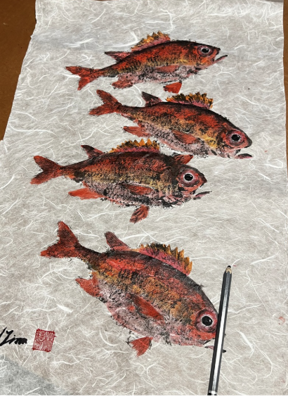 Four painted fish on paper with a paintbrush at the bottom right corner.