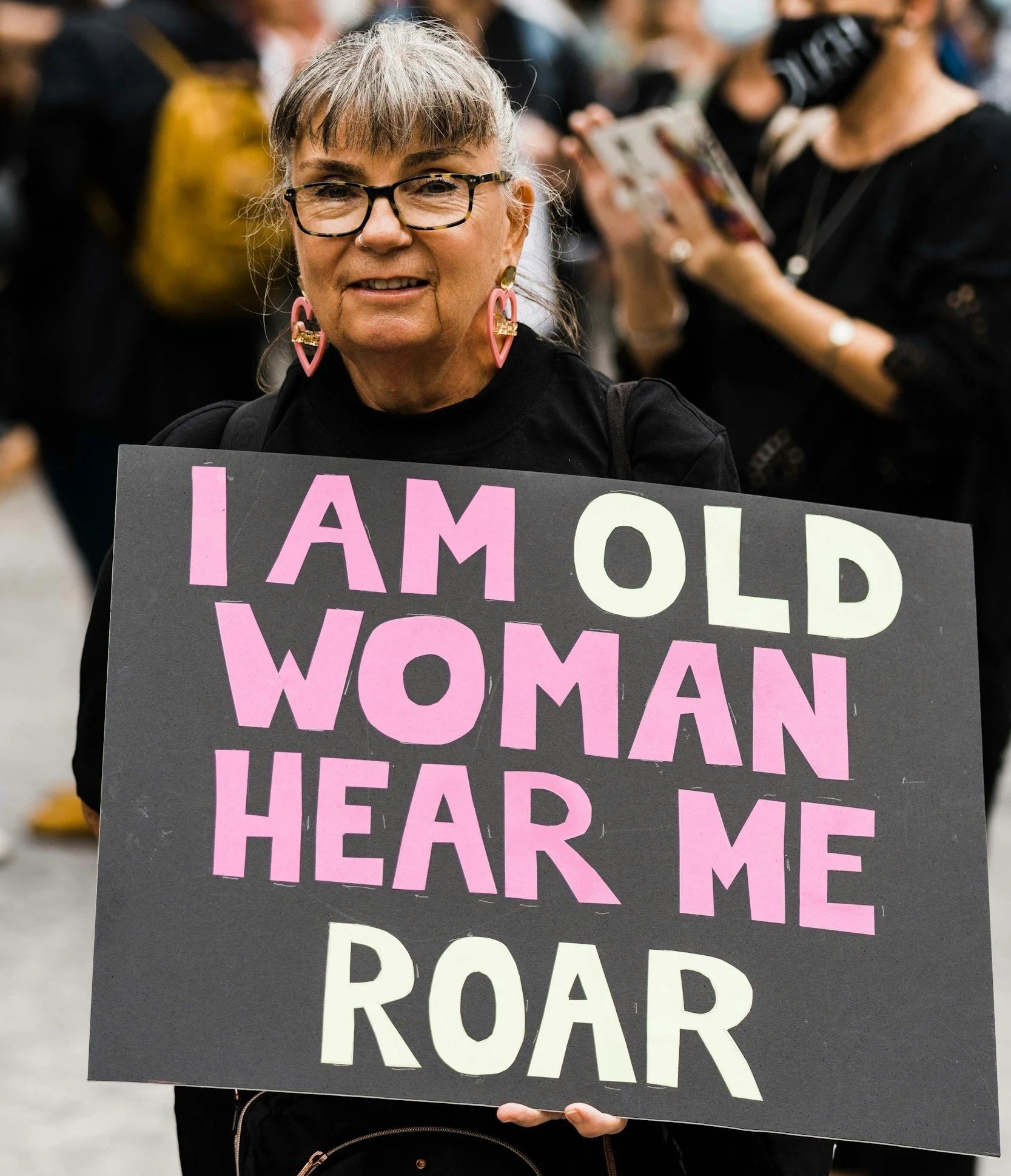 Mature woman holding sign that says "I am old woman hear me roar"