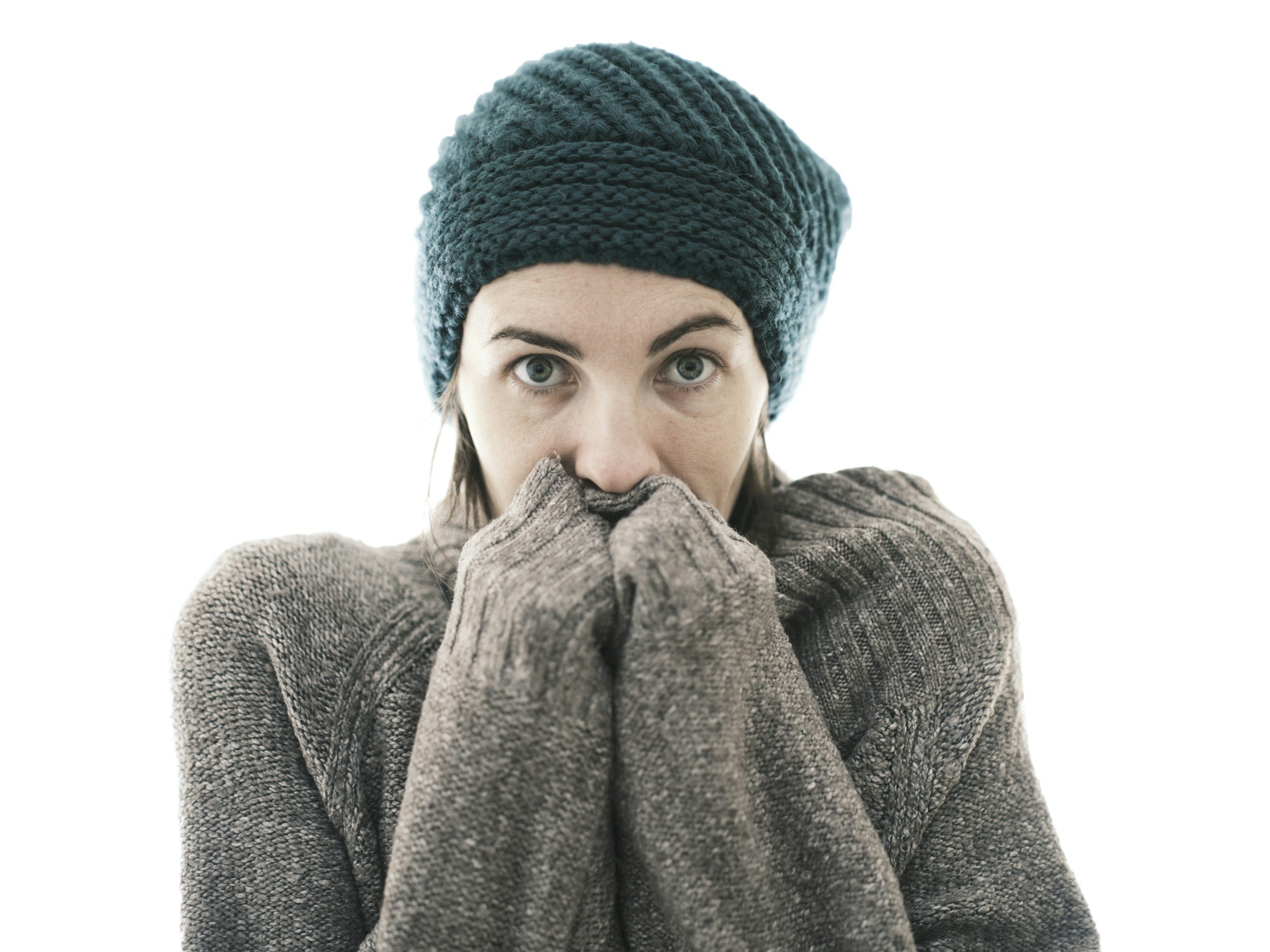 Photo of woman looking cold dressed in green wool hat with a sweater covering her hands which are covering her mouth