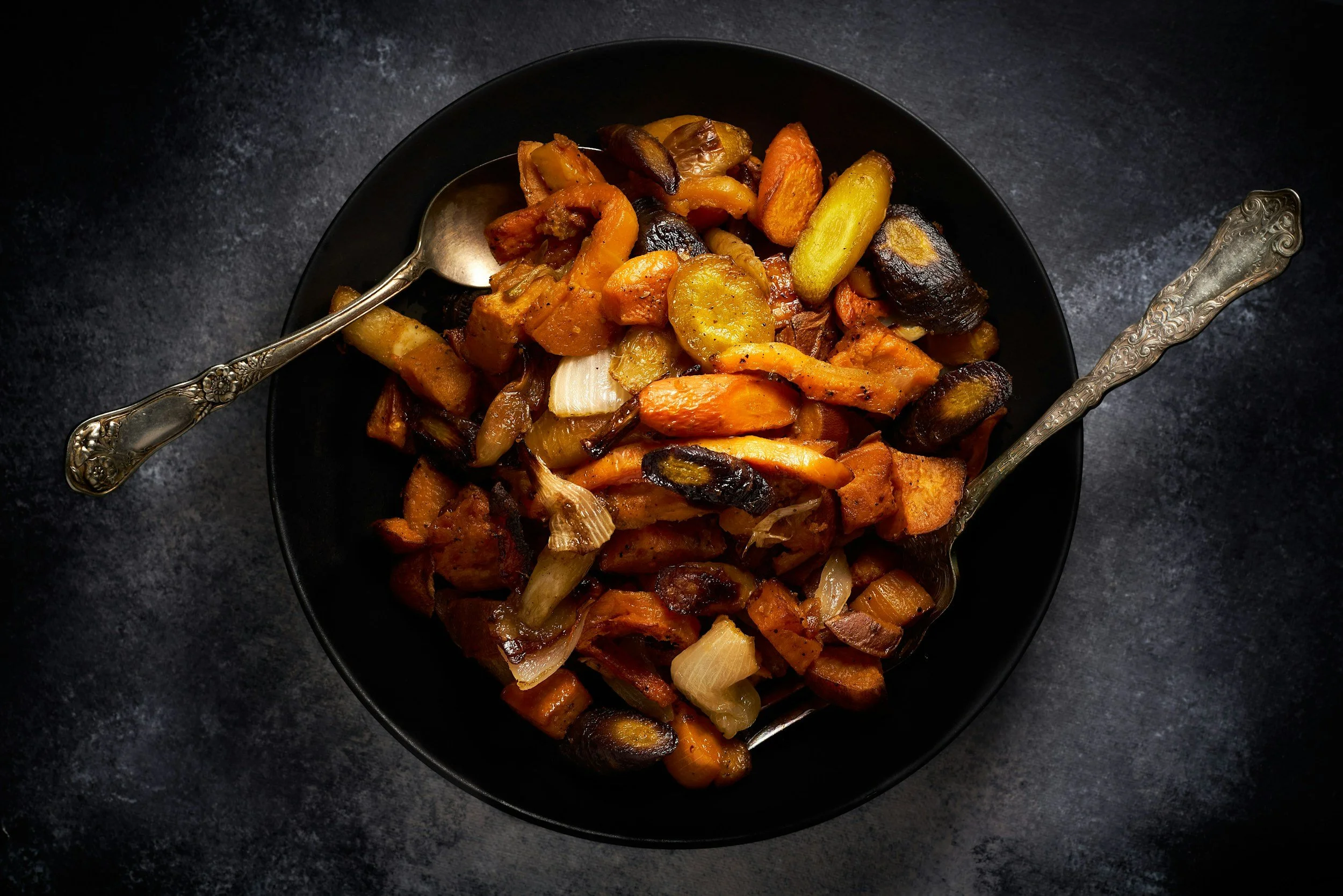 Photograph of cooked vegetables including carrot and potato in a black bowl.