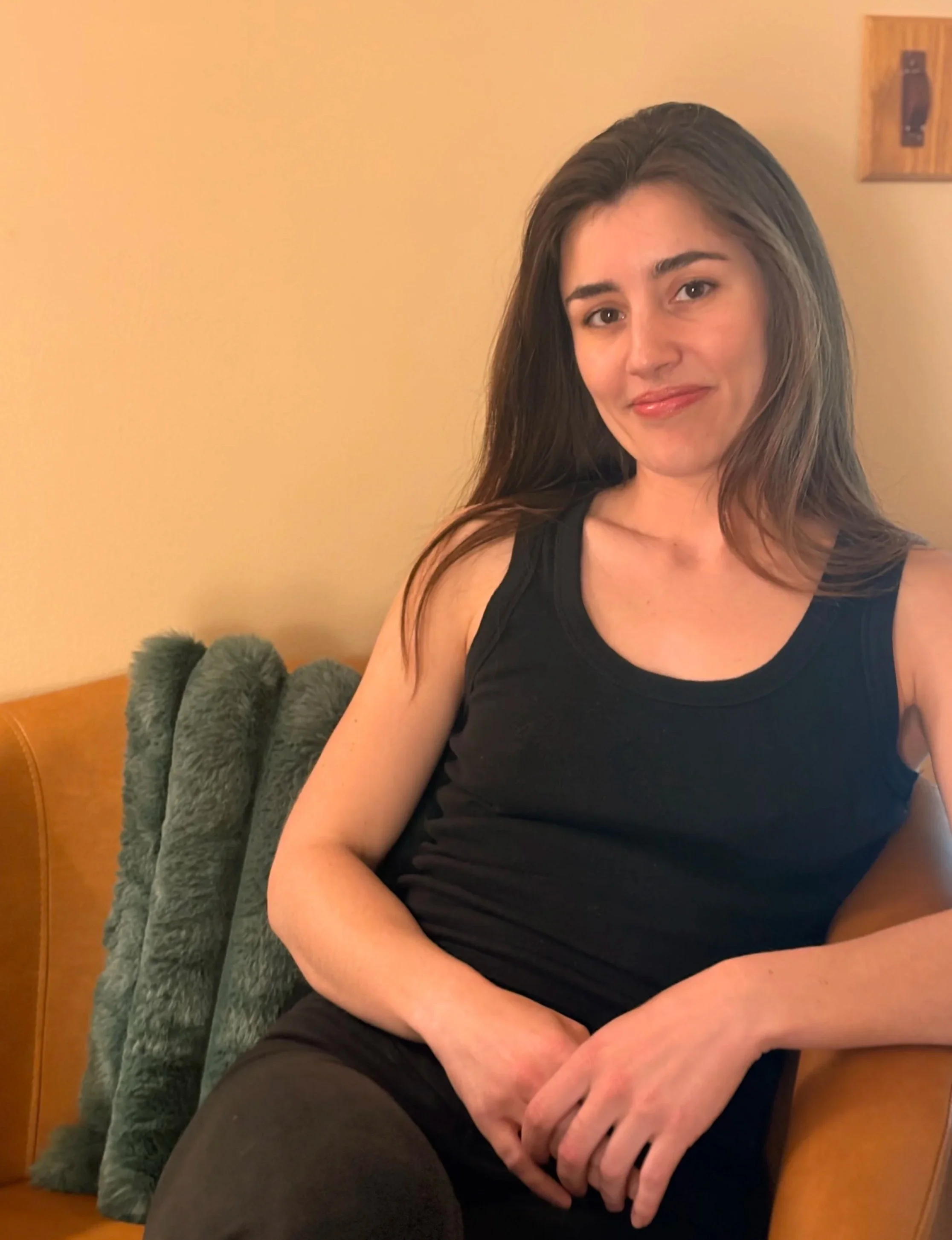 A photo of Madylan Best seated on a brown leather chair with plush green pillow behind her back.