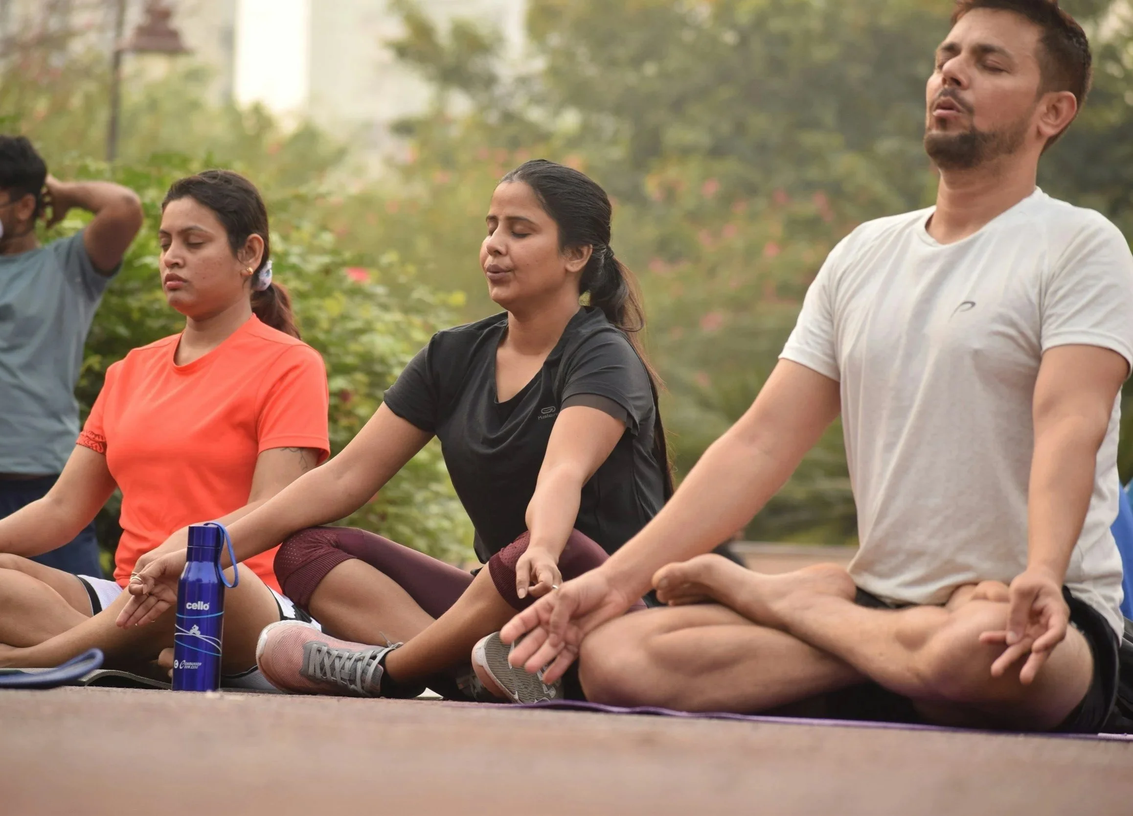 Photo of 2 women and 1 man meditating outside