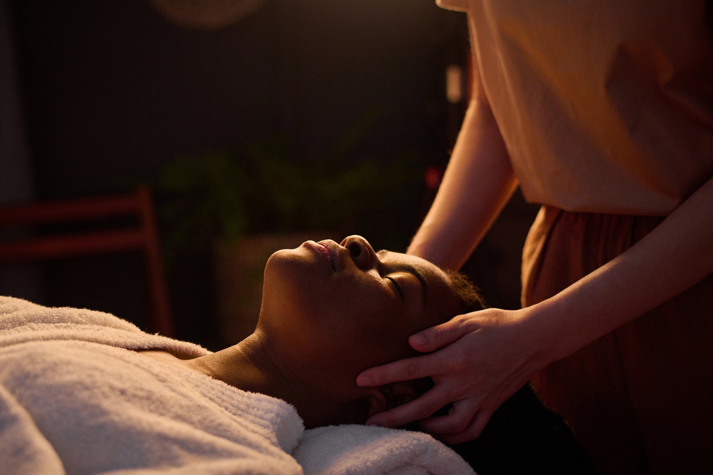 A profile of a woman's face while massage therapist holds the sides of her head.