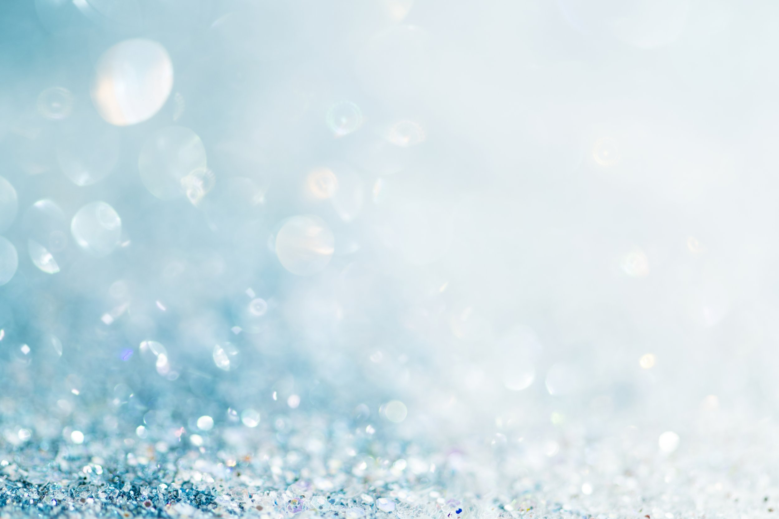 Blue and silver glitter on a surface with a bright light source and bokeh effect in the background.