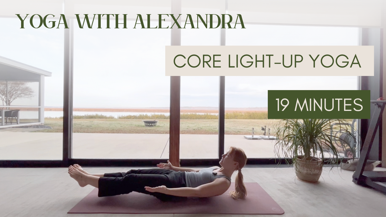 A woman doing yoga on a mat indoors by large glass windows overlooking an outdoor landscape, with text overlay reading "Yoga with Alexandra," "Core Light-Up Yoga," and "19 Minutes."