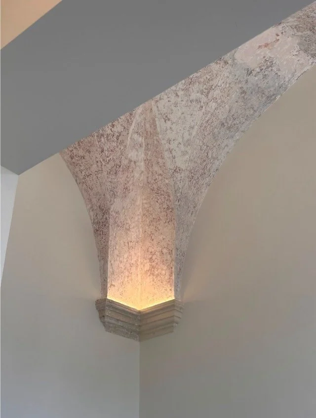 The uplighting is a modern addition, but it draws attention to something centuries older: a vault narrowing down to a single stone corbel, where the weight above comes to rest. It naturally leads the eye to one of the oldest and roughest parts of the