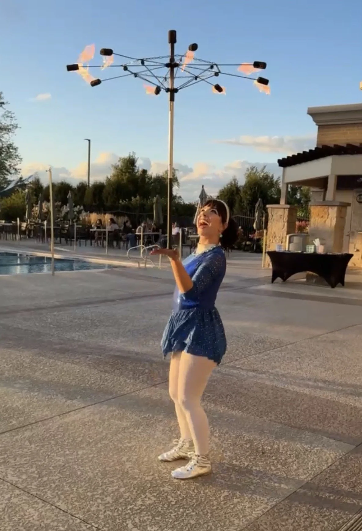 A young woman balances an umbrella that is on fire on her hand. She is wearing a blue sparkly outfit.