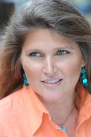 A woman with long light brown hair wearing turquoise earrings and an orange shirt, smiling slightly.