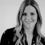 A woman with long, wavy hair wearing a dark blazer and smiling.