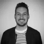 Black-and-white photo of a smiling man with short, dark hair, wearing a striped shirt and a dark jacket.