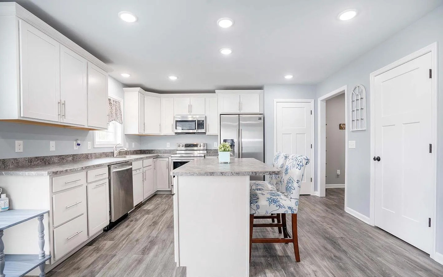 Modern kitchen with white cabinets, gray countertops, stainless steel appliances, and a small island with a floral upholstered chair.