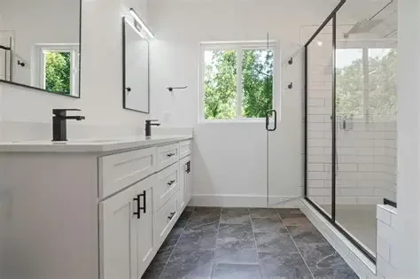 Modern bathroom with white vanity, black faucets, large mirror, walk-in shower with glass door, and window with greenery outside