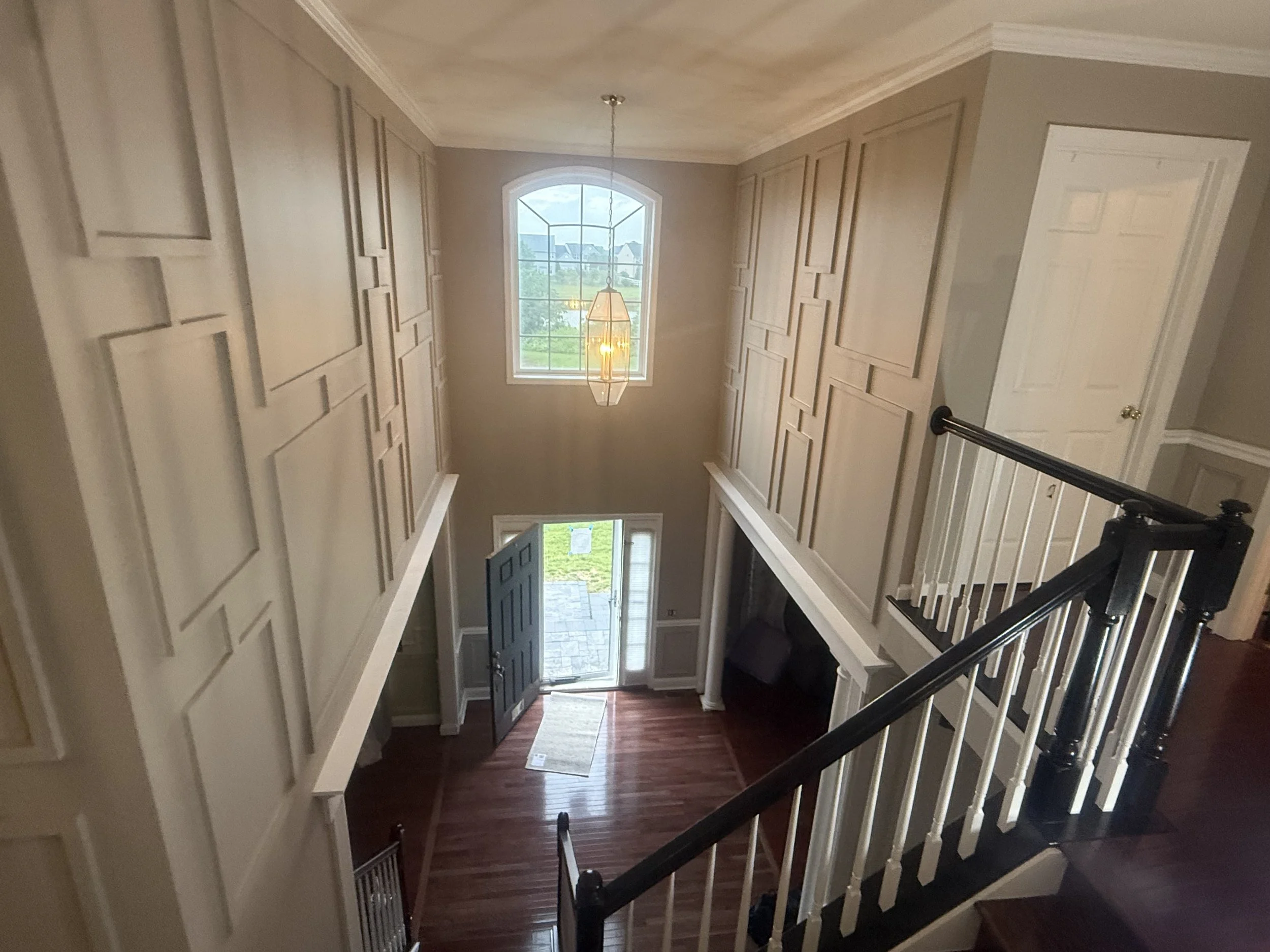 Entryway with front door, hardwood flooring, tall window, and staircase.