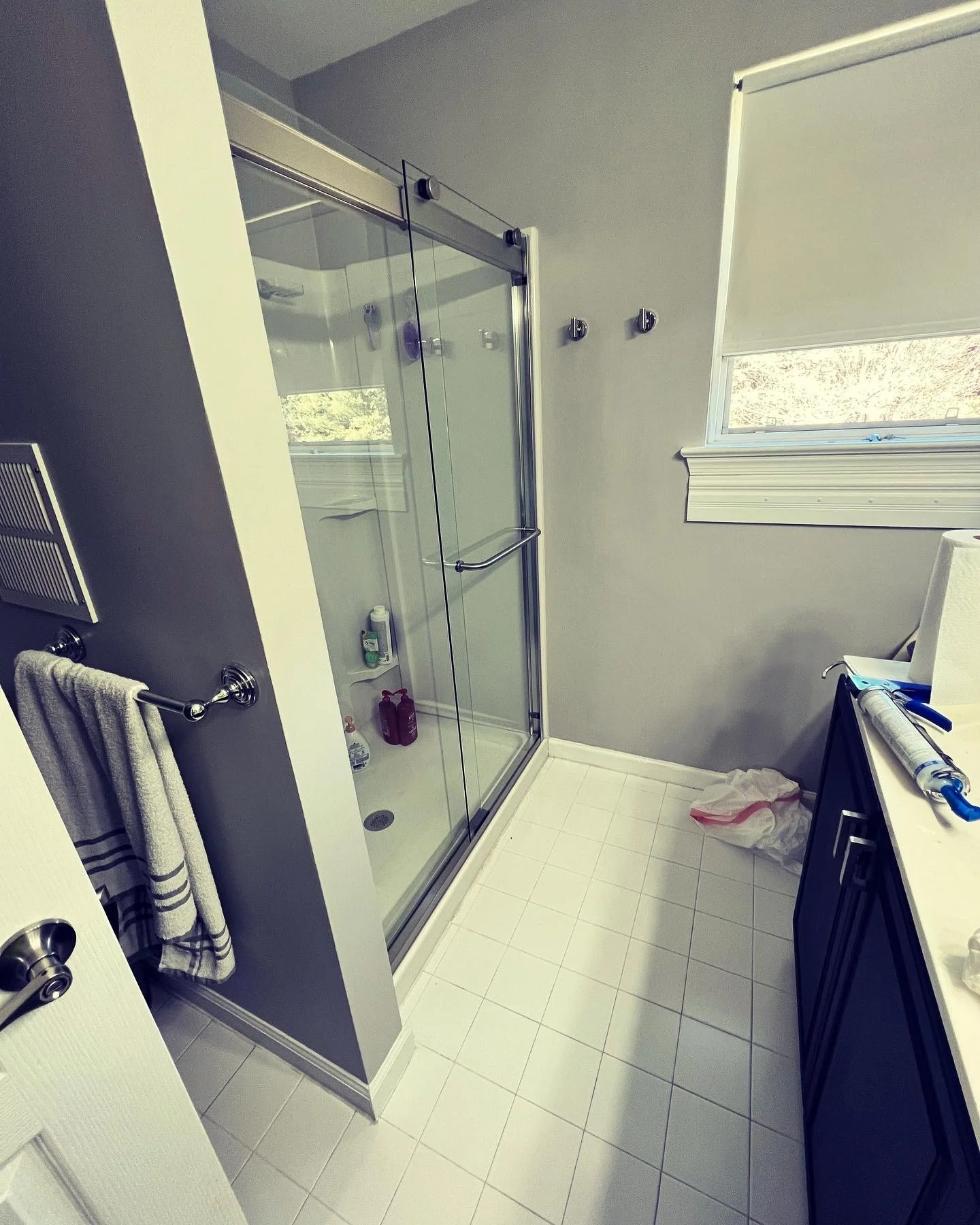 Bathroom with a glass shower stall, small window, dark blue cabinet, white countertop, towels on a towel bar, and a tissue roll.