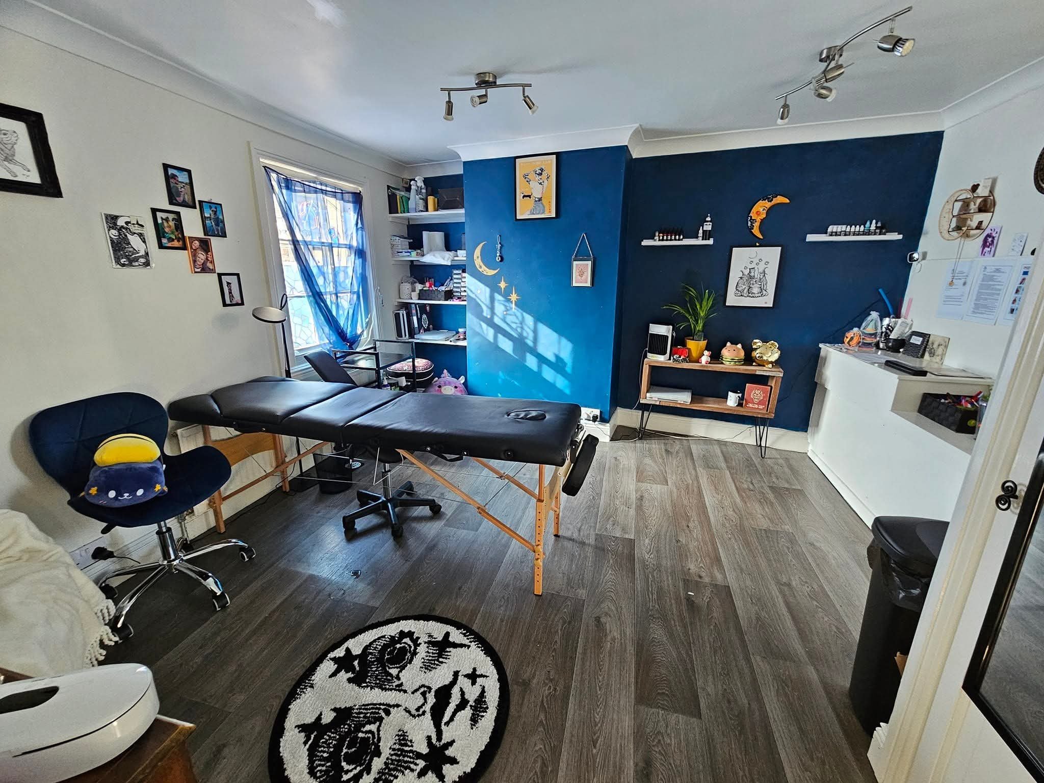 A room with a massage table, blue decorations, and various furniture and decorations including books, plants, and framed pictures.
