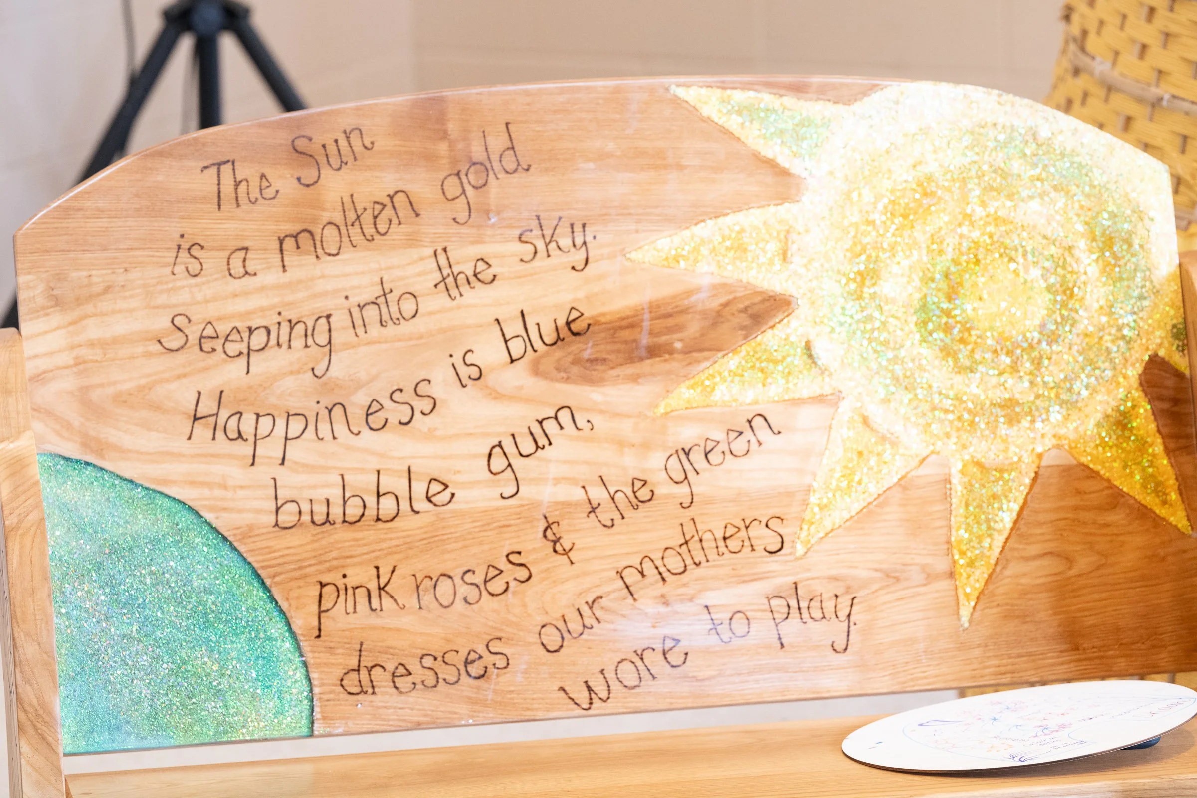 Wooden plaque with handwritten text and glittery decorations in the shape of a star and a semicircle.