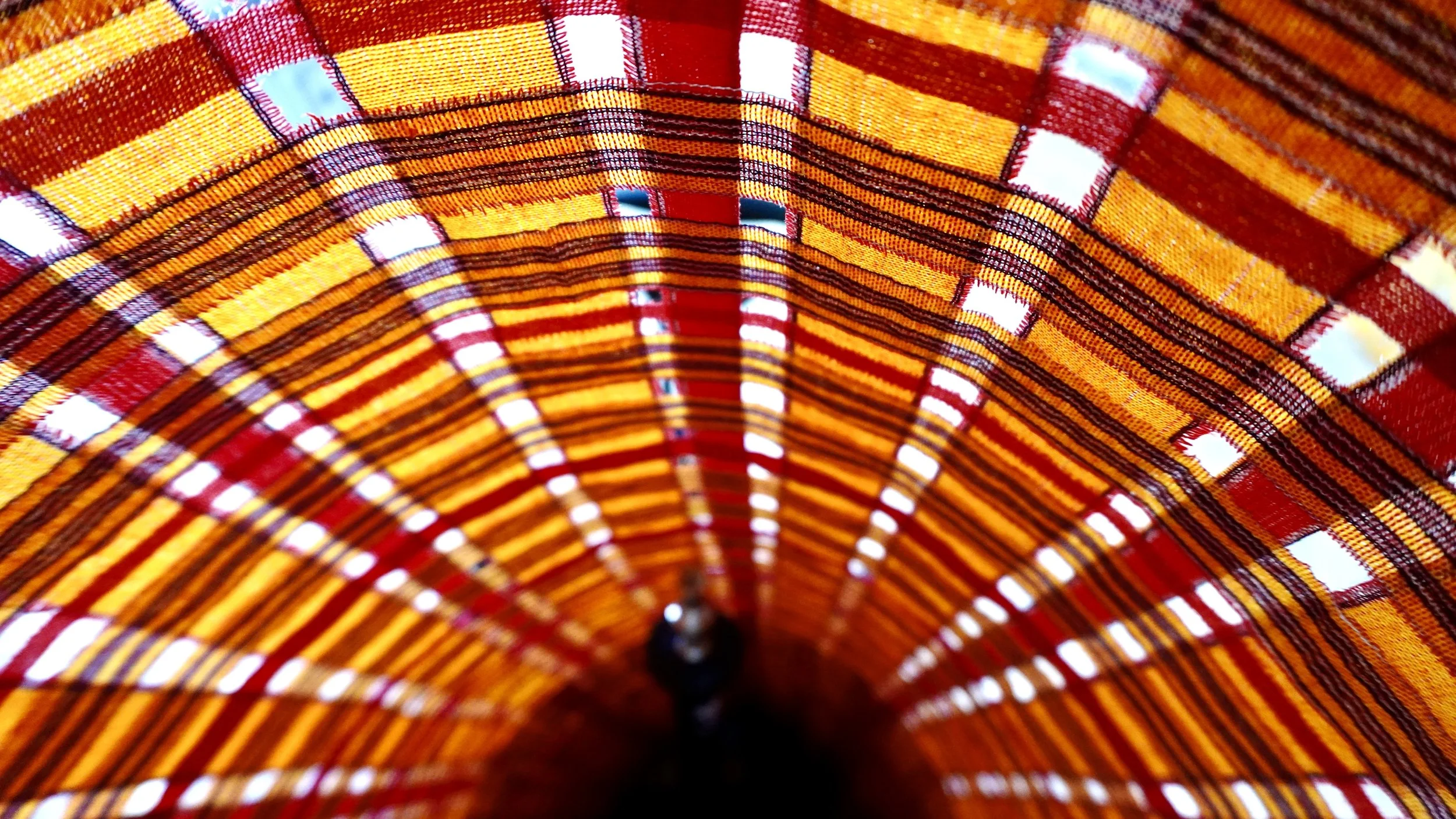 Close-up of a colorful, striped, circular fabric structure with a conical shape, featuring red, yellow, and black patterns.