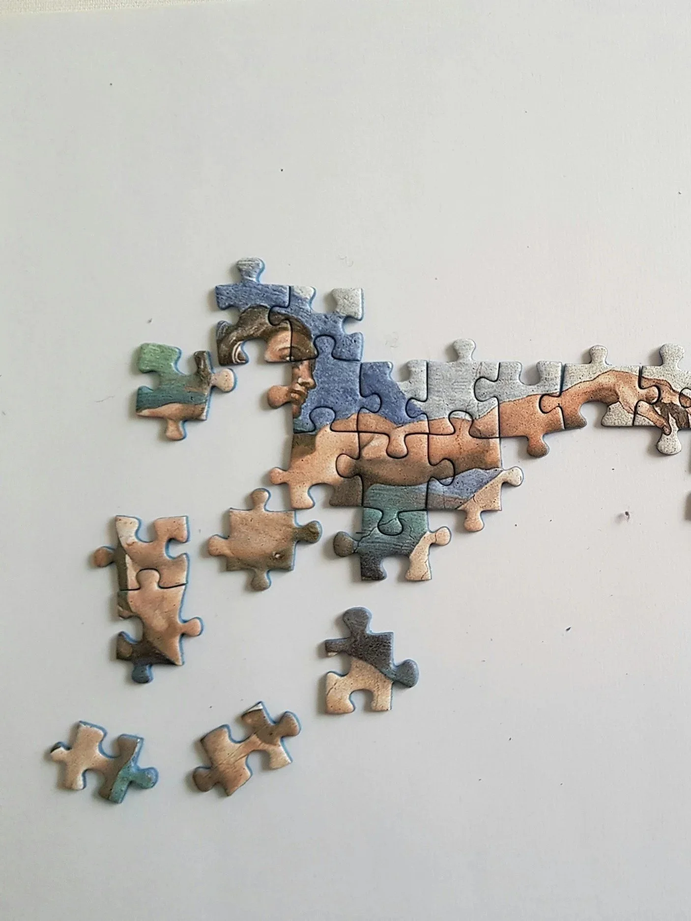 A partially assembled jigsaw puzzle depicts a face and hand, with most pieces missing, on a white surface.