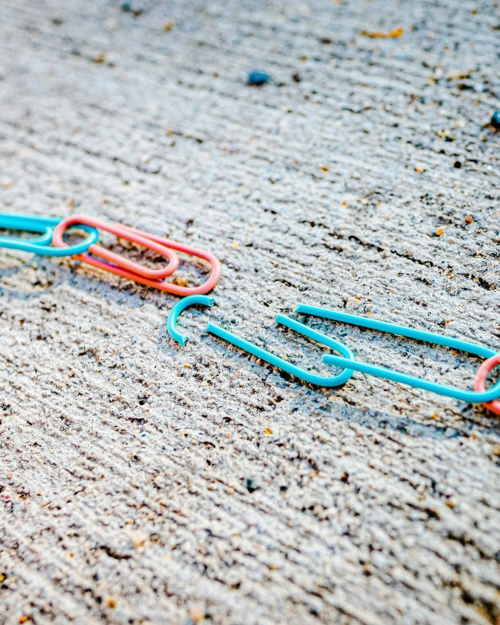 Colorful paper clips scattered on a sandy surface.